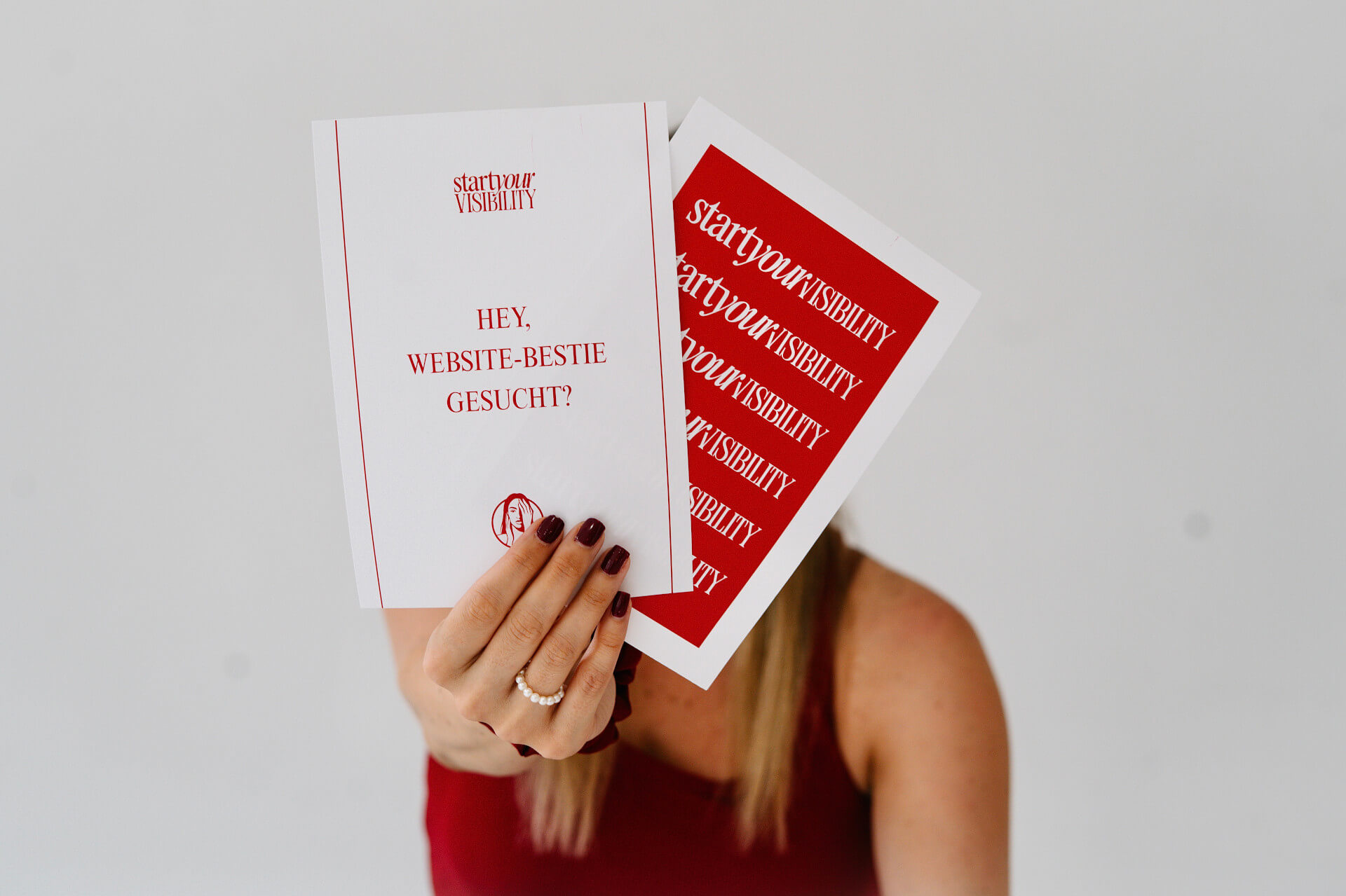 Website-Pakete-fuer-selbstaendige-Frauen Jennifer sitzt am Boden mit Schild ‚Website-Bestie gesucht?‘ in der Hand - Strategisches Webdesign für selbstständige Frauen